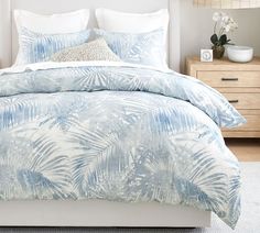 a bed covered in blue and white comforter next to a night stand with two nightstands