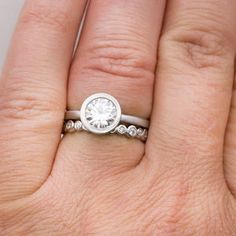 a woman's hand with a diamond ring on top of her finger and an engagement band