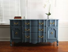 a blue dresser with gold handles in front of a window