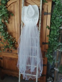 a white dress and hat hanging on a wooden door with greenery around the room