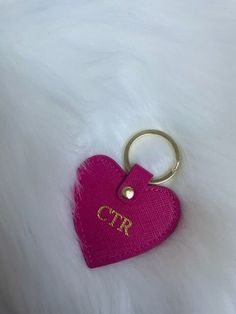 a pink heart shaped keychain sitting on top of a white fur covered surface