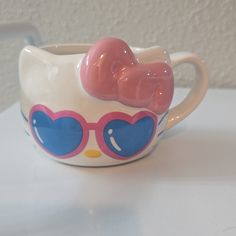 a hello kitty mug with heart shaped sunglasses on it's side and a bow at the top