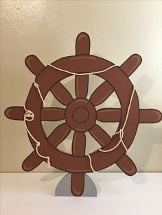 a wooden ship wheel with rope around it on a white shelf next to a wall