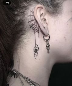 a woman's neck with spider web and cross tattoo on her left side behind the ear