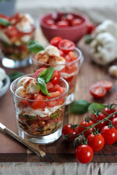 three small cups filled with food sitting on top of a wooden cutting board next to tomatoes and garlic