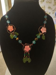 This beautiful necklace is part of the FantSea Stories collection. This necklace symbolizes the beautiful and lush gardens that flower throughout the islands. This necklace has carved pink flower beads, copper vines and swinging green leaves wrapped around delicate copper spheres. This necklace is graceful and delicate and full of beauty like the wearer of this necklace. Pink Bohemian Flower Pendant Jewelry, Bohemian Pink Flower Pendant Jewelry, Unique Copper Flower Jewelry, Artisan Green Copper Necklace, Bohemian Flower-shaped Wire Wrapped Jewelry, Bohemian Wire Wrapped Flower Jewelry, Pink Bohemian Necklace With Flower Charm, Bohemian Flower Copper Jewelry, Bohemian Pink Necklace With Flower Charm