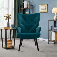 a blue chair sitting in a living room next to a table with a vase on it