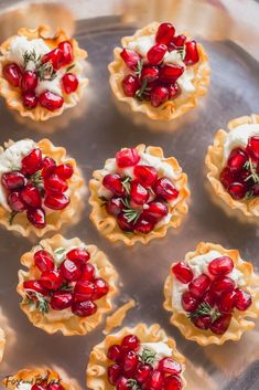 small tarts with pomegranates and whipped cream on top sit on a metal tray