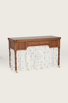 a wooden table with two drawers and a curtain on the bottom, against a white background