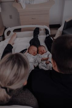 two people are laying on a bed with their babies