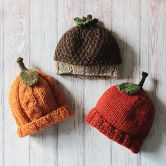 three knitted pumpkin hats sitting on top of a white wooden table next to each other