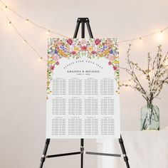 an easel with a floral wedding seating plan on it and lights in the background