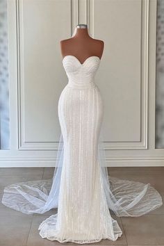 a wedding dress on display in front of a white wall and wooden mannequin