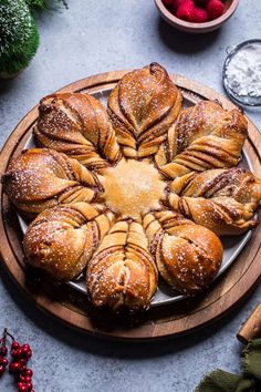 a wooden plate topped with pastries covered in powdered sugar next to bowls of raspberries