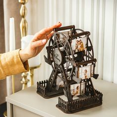 a person holding their hand up to a ferris wheel clock with pictures on the sides