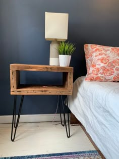 a small wooden table sitting next to a bed with a lamp on top of it