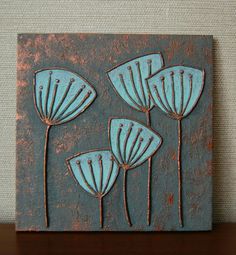 a blue and brown tile with three flowers on it's side, sitting on a shelf