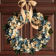 a wreath with blue and white flowers hanging on the front door, decorated with ribbon