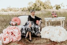 an older woman sitting on a couch surrounded by wedding dresses and bouquets in the grass