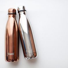 two copper colored water bottles sitting next to each other on top of a white surface