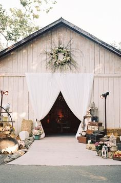 an outdoor wedding venue with white drapes and flowers on the front door, surrounded by greenery