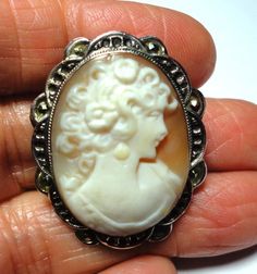 Cameo brooch pin is a Vintage antique Italian cameo pin in a solid sterling silver frame with marcasites on the mounting. Genuine vintage carved shell cameo in solid sterling silver frame mounting with marcasites adding sparkle and embellishing the ornate cameo frame. This lovely vintage cameo treasure, is a a genuine hand carved shell cameo, and it can be worn as a brooch or pendant. The cameo is signed by the artist on the back. There is a loop for a chain or ribbon on the back. The back frame Antique Carved Brooches For Weddings, Antique Cameo Brooches For Wedding, Ornate Carved Oval Brooches, Ornate Oval Carved Brooches, White Cameo Brooch For Wedding, White Cameo Brooches For Wedding, Antique Oval Carved Brooches, Vintage Intaglio Brooches For Anniversary, White Cameo Wedding Brooches