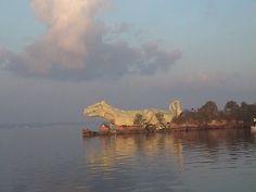 a large body of water with a statue on it's side and clouds in the background