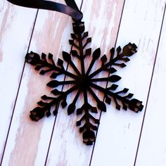 a metal snowflake hanging from a ribbon on a white wooden wall with planks