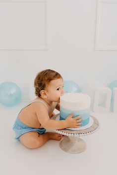 a baby sitting on the floor with a cake in front of him and looking at it