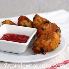 some fried food on a white plate with ketchup in a small bowl next to it