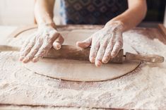 a person rolling dough on top of a wooden table