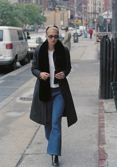 a woman is walking down the sidewalk with her cell phone in her hand and she's wearing a black coat