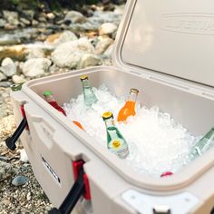 an ice chest filled with bottles of beer on the ground next to rocks and water