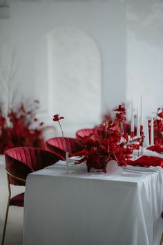 the table is set with white linens and red flowers in vases on each side