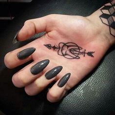 a woman's hand with an arrow tattoo on her left thumb and black nails