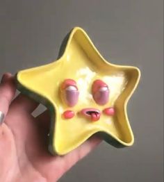 a hand holding a yellow star shaped bowl with eyes and nose painted on it's side