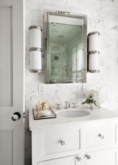 a bathroom with marble counter tops and white cabinetry, along with a large mirror above the sink