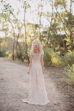 a woman in a wedding dress walking down a dirt road