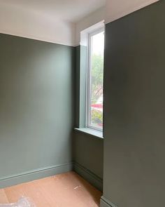 an empty room with green walls and wood flooring in the foreground, there is a plastic bag on the floor next to the window