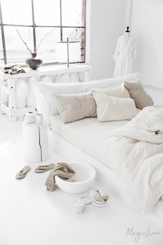 a white bed sitting in a bedroom next to a window with lots of pillows and blankets on top of it