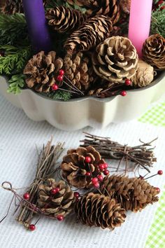 pine cones, berries and candles are arranged in a bowl on a table with green checkered cloth