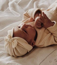 a baby laying on top of a bed wearing a sweater and holding a finger up