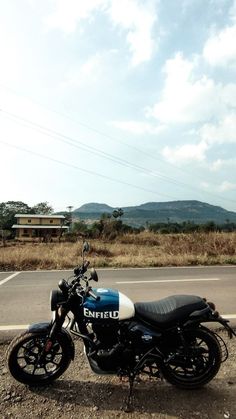 a motorcycle is parked on the side of the road in front of a field and mountains