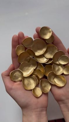 two hands holding gold discs in front of a white wall