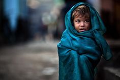 a young boy wrapped in a blue blanket on the street, looking at the camera