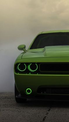 the front end of a green car with its lights on and fog in the background