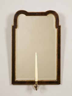 a mirror mounted on the wall with a candle in it's center and an ornate wooden frame