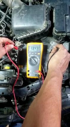 a man working on an electronic device under the hood of a car with wires attached to it