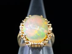 This ring is a classic piece that features an eye-catching opal stone surrounded by a sleek yellow gold band. The sophisticated styling and elegant color combination make this ring perfect for any occasion.Metal: 10K Yellow GoldGem: Opal 5.02 CaratsGem Measurements: 12.4 x 16.2 mm, OvalRing Size: 6.25Marks: "10K" Stamped on the inside band Classic Yellow Gold Opal Ring, Formal Yellow Gold Ethiopian Opal Ring, Formal Ethiopian Opal Cabochon Ring, Opal Solitaire Ring, Elegant Color, Opal Stone, Gold Band, Color Combination, Solitaire Ring