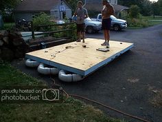 two people standing on top of a wooden platform in the middle of a driveway next to a house